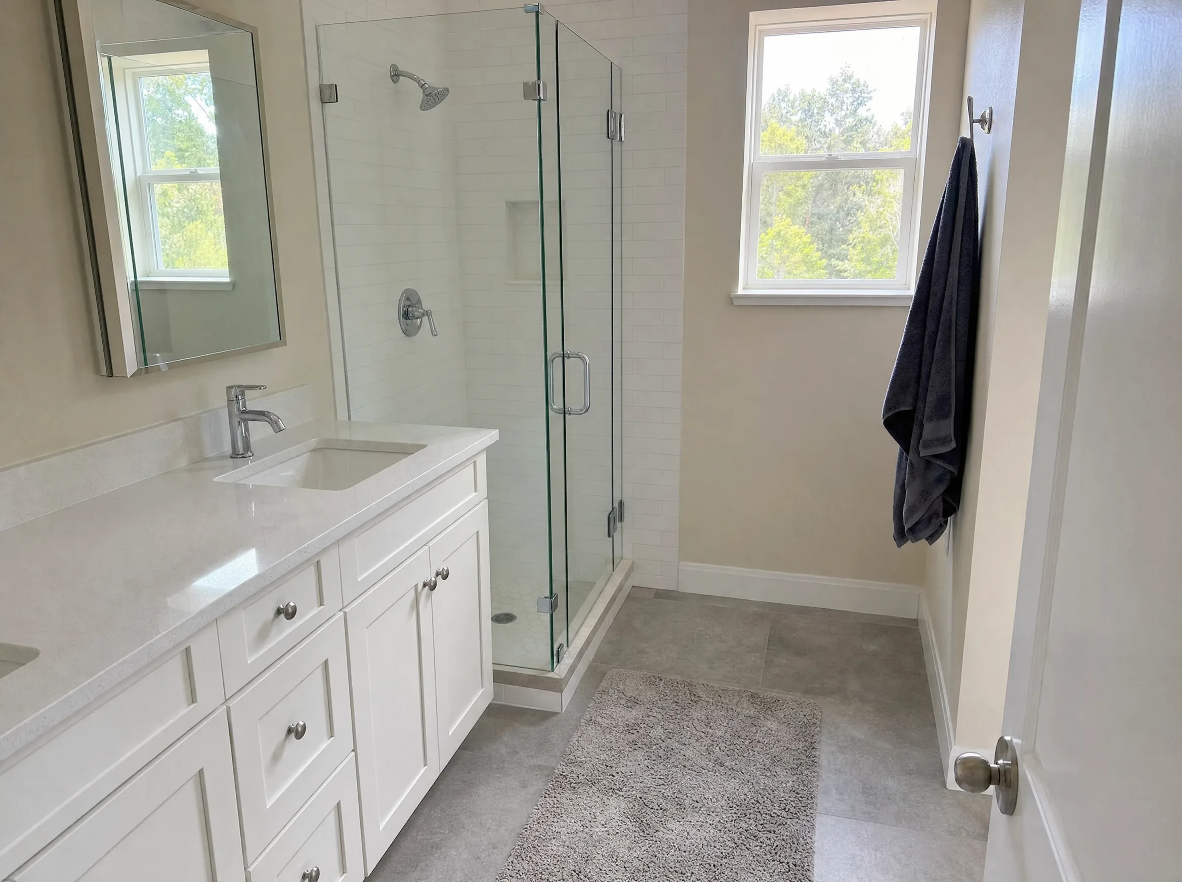 Remodeled bathroom with a white shaker vanity, quartz top, large-format floor tile and a glass shower