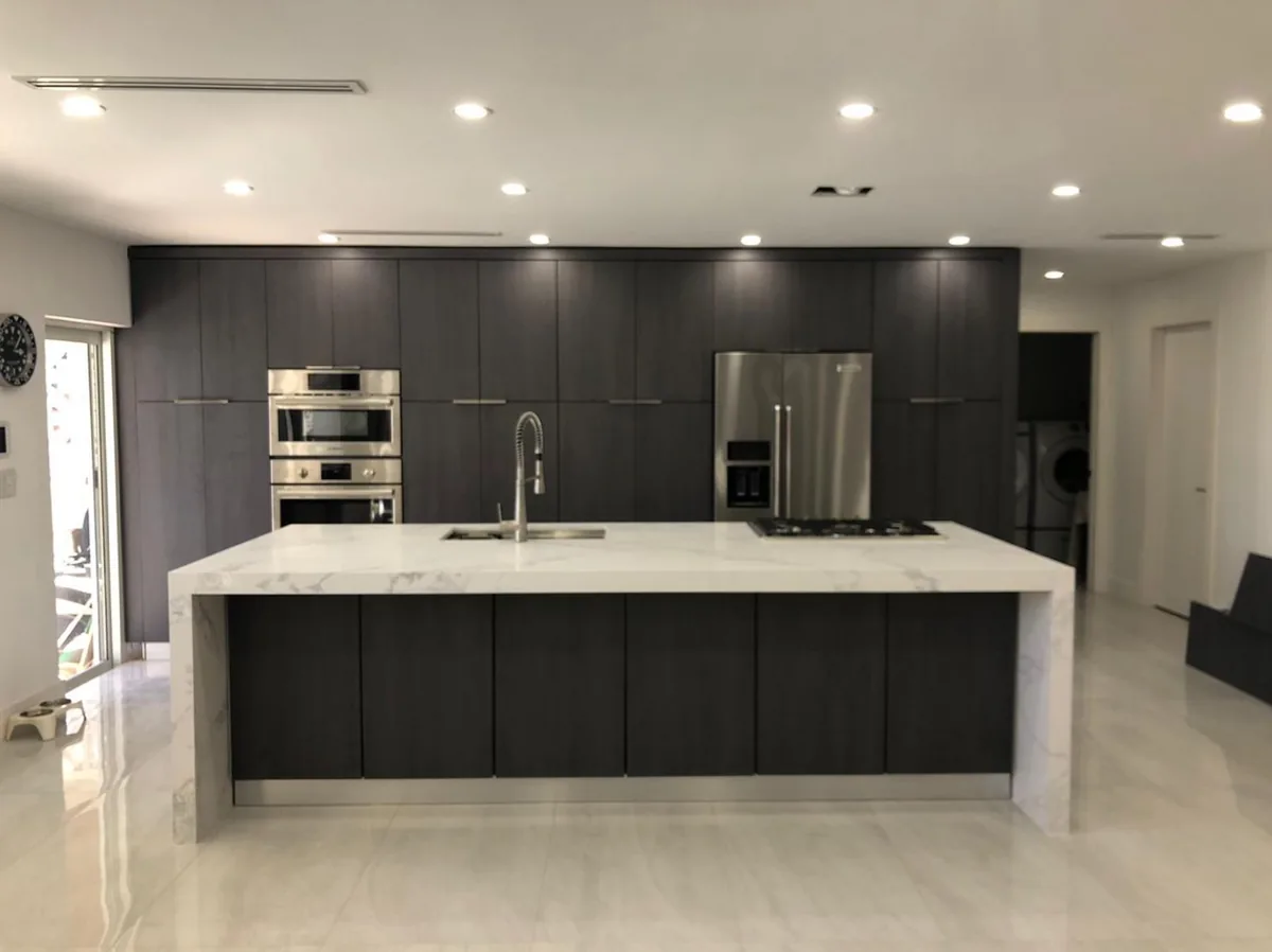 Long white quartz waterfall island in front of a dark cabinet wall with stacked wall ovens